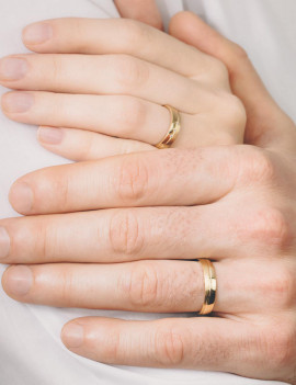 Primer plano de las manos de una pareja luciendo sus anillos de oro amarillo a juego.