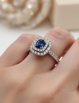 Anillo de zafiro azul ovalado y diamantes halo doble en oro blanco 18k puesto en la mano de una mujer, mostrando escala y brillo