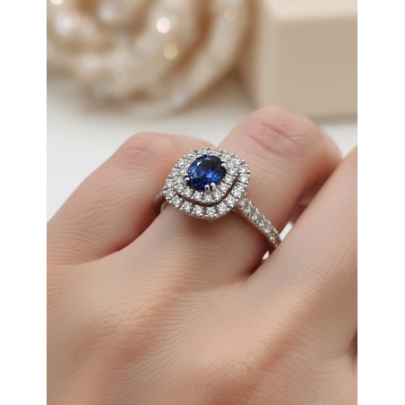 Anillo de zafiro azul ovalado y diamantes halo doble en oro blanco 18k puesto en la mano de una mujer, mostrando escala y brillo