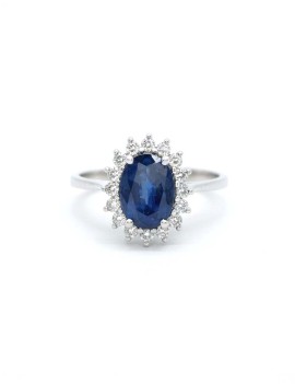 Anillo Victoria con un zafiro ovalado azul central rodeado por dieciséis diamantes de talla brillante de oro amarillo 18k.